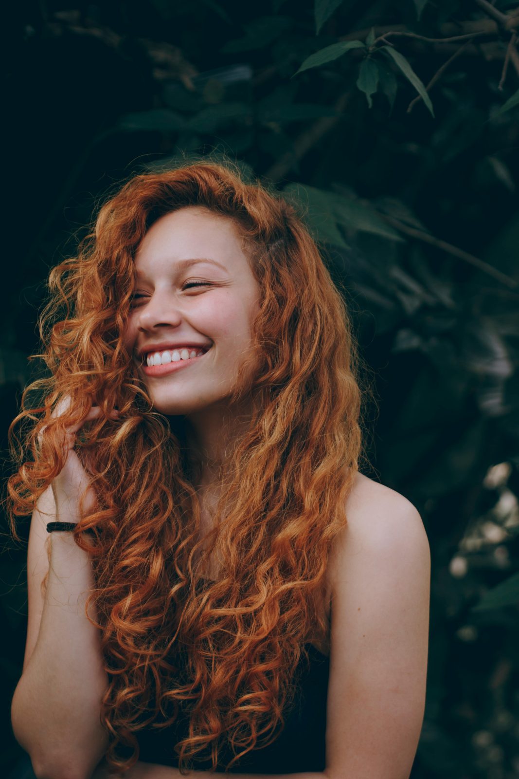 A candid portrait of a joyful woman with curly red hair, expressing natural beauty and happiness.