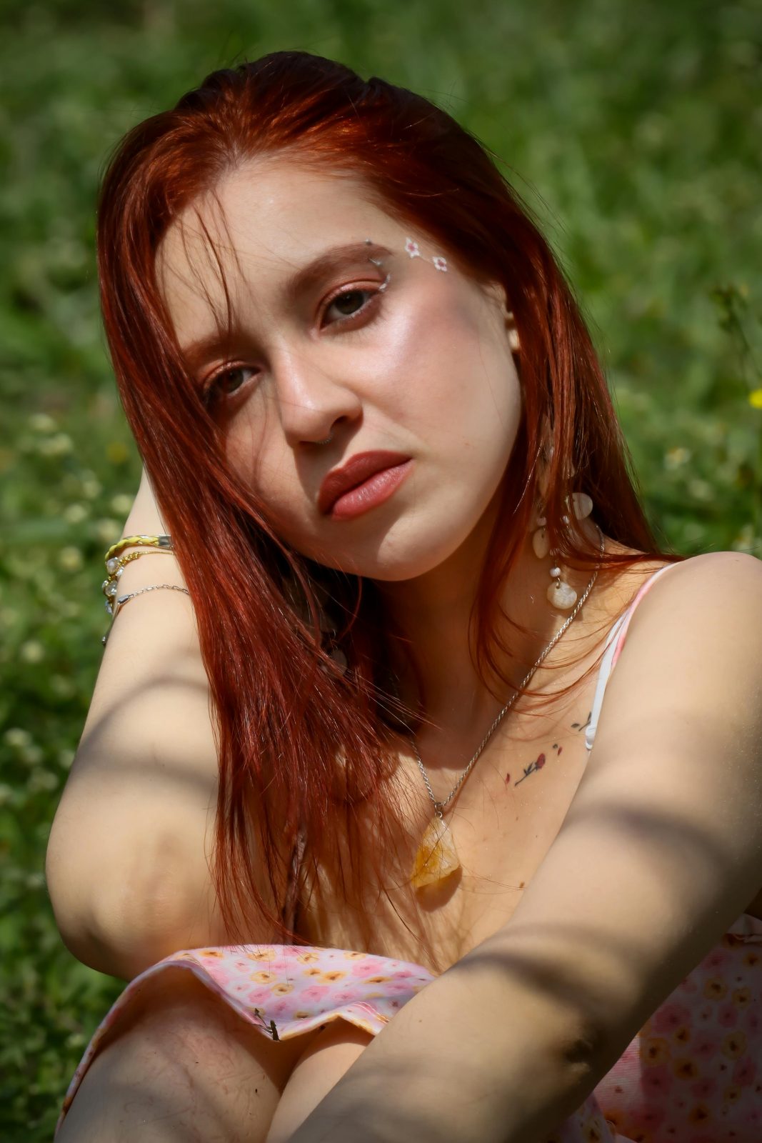 Close-up portrait of a woman with red hair sitting in a sunlit garden.